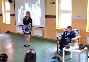 Dziewczynka z kapeluszem w dłoni, improwizuje śpiew do mikrofonu. Za nią wyświetlany jest fragment oryginalnego wykonania.
