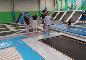 Grupka uczniów strojach sportowych czeka na skoki przed tramploiną.
