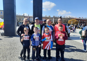 Uczniowie reprezentujący szkołę w biegu wraz z rodzicami pozują do zdjęcia prezentując zawieszone na szyi medale.