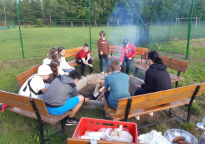Uczniowie pieką kiełbaski nad ogniskiem.