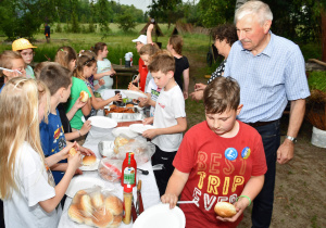 Uczniowie przy stole plenerowym z jedzeniem przygotowanym na ognisko.