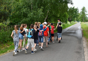 Uczniowie maszerują za wychowawczynią po drodze.