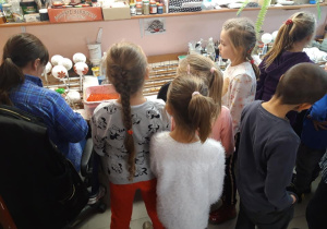 Dzieci przyglądają się pracy pani dekorującej ozdoby choinkowe.