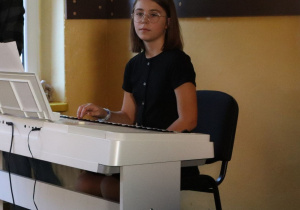 Uczennica klasy trzeciej siedzi przy pianinie. Czeka na odegranie utworów dla nauczycieli.