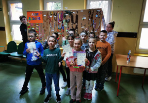 Uczniowie nagrodzeni w konkursie prezentują otrzymane nagrody i dyplomy. W tle tablica z pracami konkursowymi.