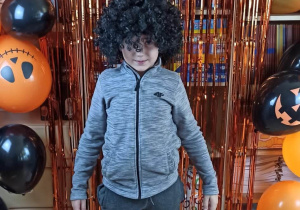 Chłopiec w czarnej peruce pozuje na tle dekoracji Halloweenowej.