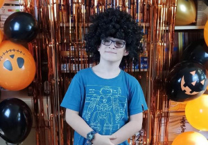Chłopiec w czarnej peruce pozuje na tle dekoracji Halloweenowej.