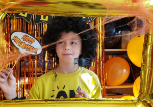 Uczeń pozuje do zdjęcia w ramce z gadżetami Halloweenowymi.