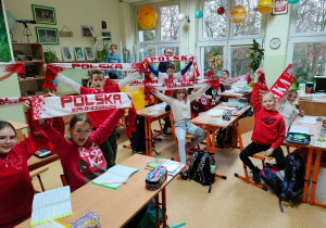 Uczniowie klasy czwartej w barwach narodowych pozują do zdjęcia w sali przyrodniczej wraz z nauczycielem.
