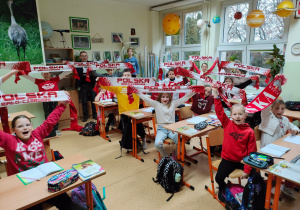 Uczniowie klasy czwartej w barwach narodowych pozują do zdjęcia w sali przyrodniczej wraz z nauczycielem.