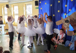 Uczniowie z klasy trzeciej przebrani za śnieżynki tańczą na szkolnym holu układ taneczny.