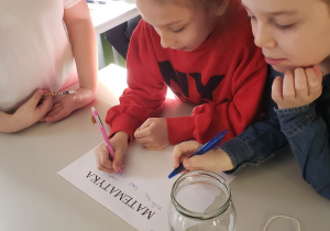 Grupa uczniów siedzi przy stoliku rozwiązując wspólnie zadanie matematyczne.