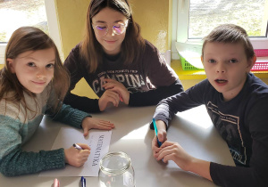 Grupa uczniów siedzi przy stoliku rozwiązując wspólnie zadanie matematyczne.