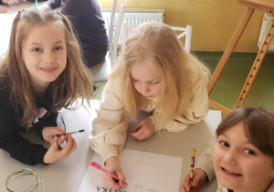 Grupa uczniów siedzi przy stoliku rozwiązując wspólnie zadanie matematyczne.