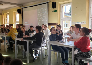 Grupa uczniów siedzi przy stoliku rozwiązując wspólnie zadanie matematyczne.