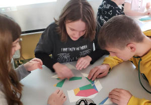 Grupa uczniów siedzi przy stoliku rozwiązując wspólnie zadanie matematyczne.