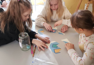 Grupa uczniów siedzi przy stoliku rozwiązując wspólnie zadanie matematyczne.