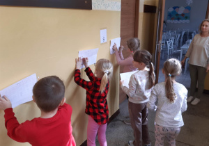Uczniowie rozwiązują łamigłówki matematyczne przyczepione na ścianie korytarza szkolnego.