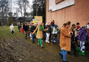 Uczniowie szkoły w kolorowych strojach maszerują radośnie w pochodzie wiosennym.