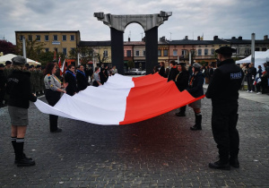 Harcerze z wielką biało-czerwoną flagą na tle pomnika na placu 11 Listopada w Łasku