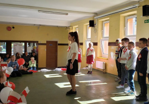 Uczennica klasy piątek deklamuje wiersz podczas apelu z okazji 3 Maja.