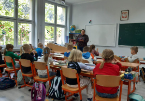 Uczniowie w ławkach słuchają pani bibliotekarki.