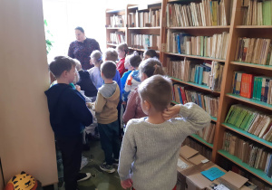 Uczniowie między półkami w bibliotece szkolnej.