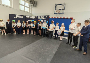 Uczniowie klasy trzeciej w wakacyjnych strojach podczas przedstawienia artystycznego.