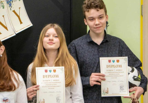 Uczeń i uczennica dumnie prezentują dyplomy otrzymane w konkursie polonistycznym.