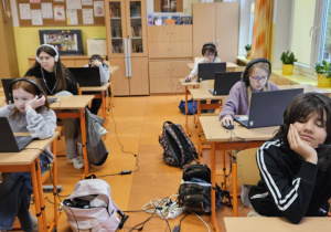Uczniowie ze słuchawkami na uszach rozwiązują zadania konkursowe na laptopach.