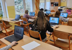 Uczniowie ze słuchawkami na uszach rozwiązują zadania konkursowe na laptopach.