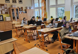 Uczniowie ze słuchawkami na uszach rozwiązują zadania konkursowe na laptopach.