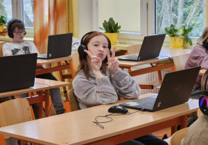 Uczniowie ze słuchawkami na uszach rozwiązują zadania konkursowe na laptopach.