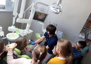 Uczeń siedzi na fotelu dentystycznym. Higienistka za pomocą kamery pokazuje uśmiech ucznia na ekranie.