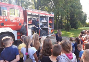 Dzieci słuchają strażaków i oglądają wyposażenie wozu strażackiego.