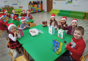 Dzieci z oddzialu przedszkolnego siedząc przy stolikach jedzą babeczki.