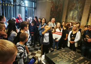 Uczestnicy wycieczki gromadzą się w kościele słuchając w skupieniu przewodnika wyciceczki.