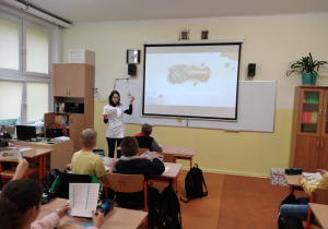 Pani dietetyk stoi przed uczniami, za jej plecami widać ekran na ścianie z logo akcji Zdrowa Klasa.