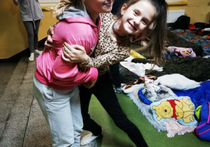 Uczennice klasy czwartej pozują do zdjęcia, w tle widać materace i śpiwory rozłożone na podłodze na szkolnym korytarzu.