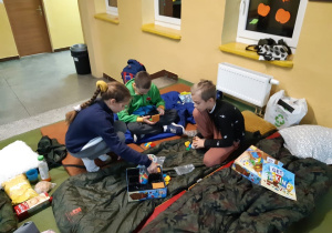 Grupka uczniów klasy trzeciej gra w grę planszową na materacach podczas nocowania w szkole