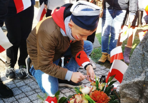 Uczeń klasy 5 zapala znicz przy pomniku walczących o niepodległość Polski.
