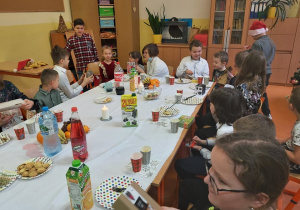 Uczniowie klasy piątej i pierwszej siedzą przy wigilijnym stole, pokazują sobie nawzajem otrzymane właśnie przezenty.