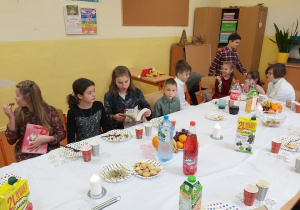 Uczniowie klasy piątej i pierwszej siedzą przy wigilijnym stole, pokazują sobie nawzajem otrzymane właśnie przezenty.