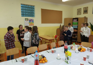 Uczniowie łamią się opłatkiem. Na pierwszym planie widać stół wigilijny.