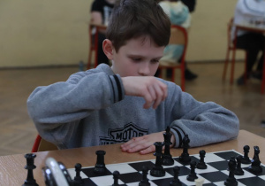 Uczeń przy stole szachowym przygląda się w skupieniu planszy i pionkom.