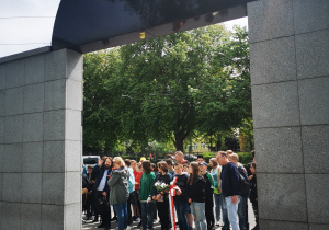 Uczniowie gromadzą się przed pomnikiem ofiar Holocaustu wraz z przewodnikiem.