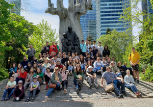 Uczestnicy wycieczki pozują do zdjęcia grupowego przy pomniku Janusza Korczaka w Warszawie.