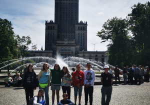 Uczniowie pozują do zdjęcia grupowego przed Pałacem Kultury i Nauki w Warszawie. W tle widać fontannę.