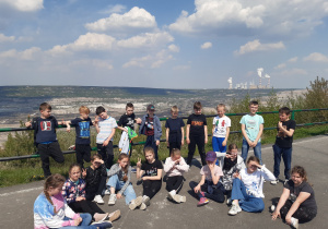 Uczniowie pozują do zdjęcia na tarasie widokowym, w tle krajobraz po wydobyciu węgla oraz kominy z kopalni Bełchatów.