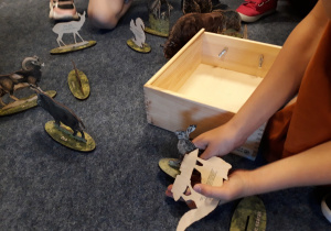 Dziecko bawi się drewnianymi figurkami zwierząt na dywanie.